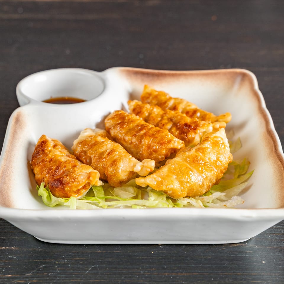 Golden-brown dumplings served on shredded lettuce with a small dish of dipping sauce.